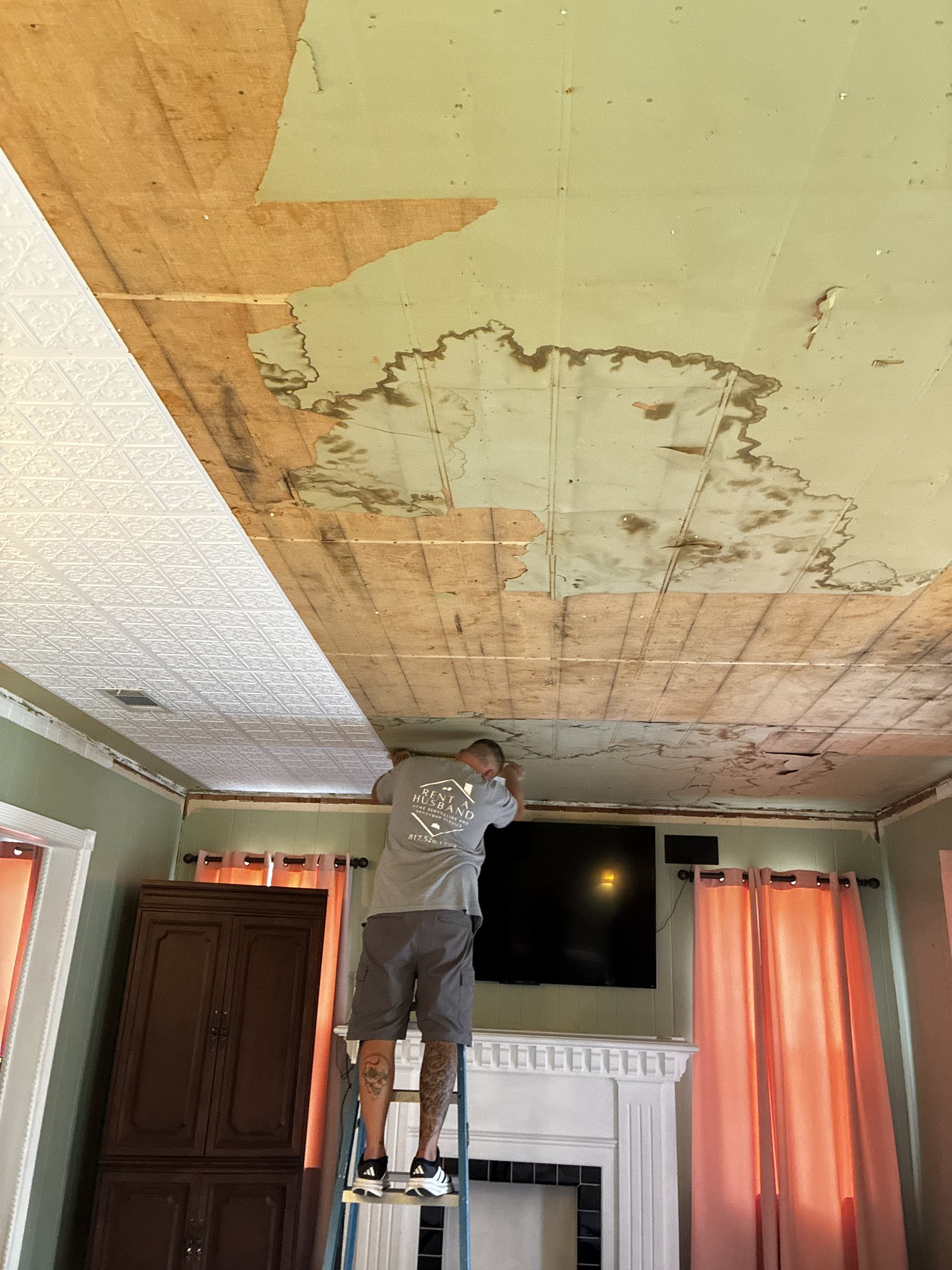 Worker removing damaged ceiling material above a living room fireplace.