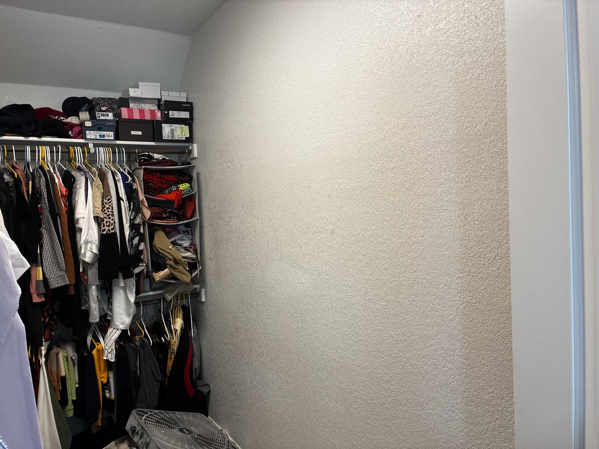 Repaired textured closet wall beside hanging clothes and storage shelves.