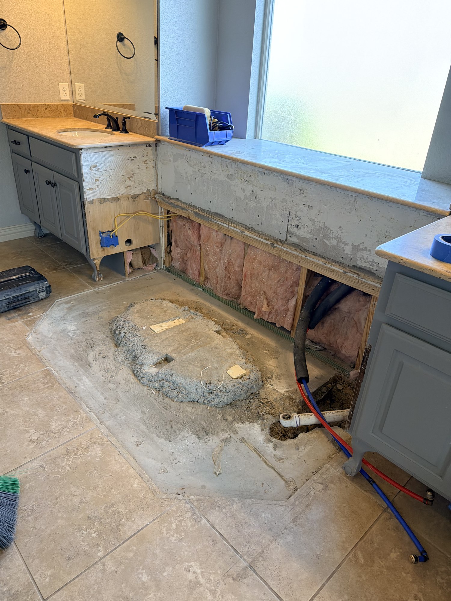 Close view of exposed plumbing, insulation and floor preparation beneath a bathroom window.