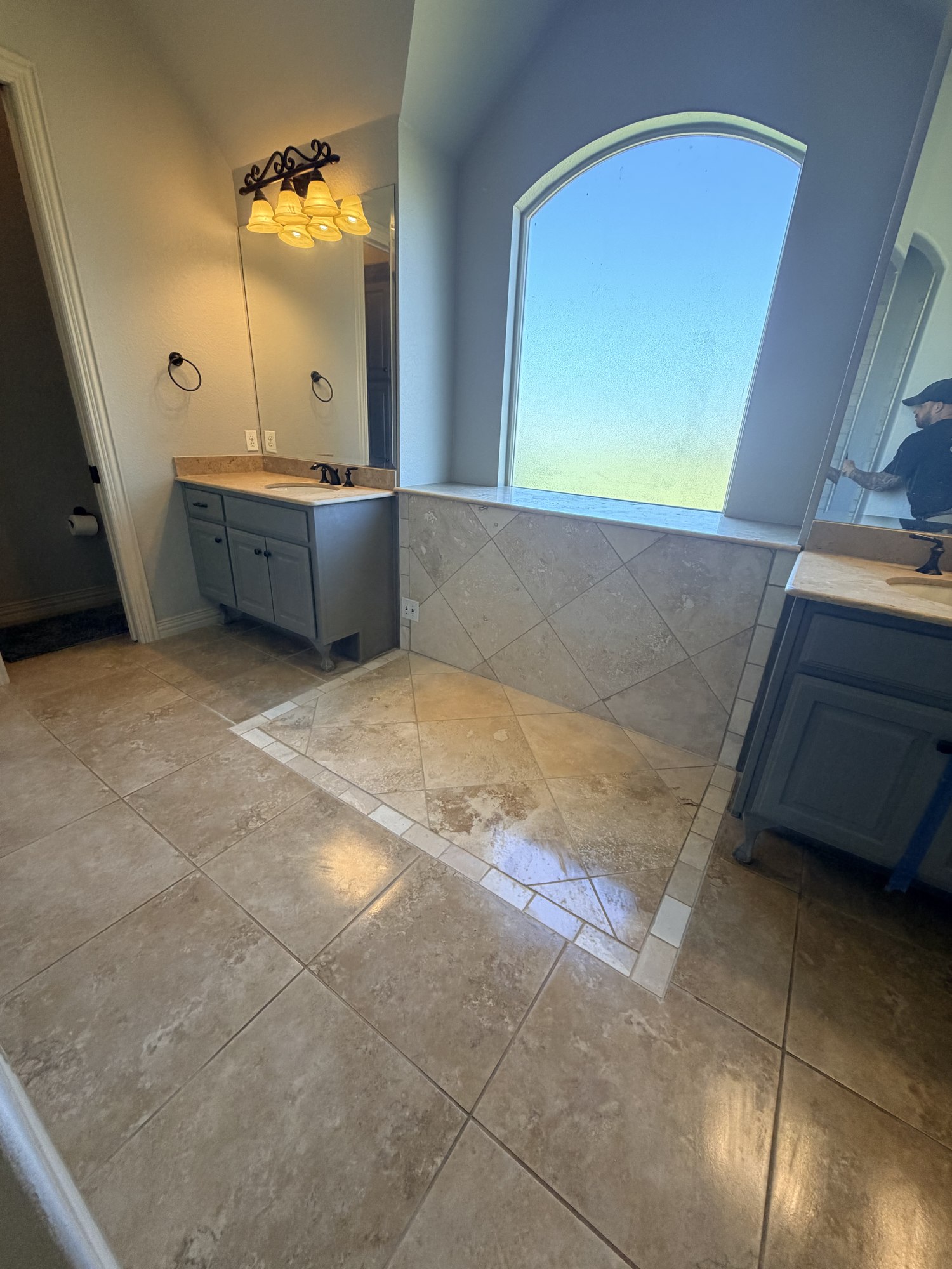 Alternate view of bathroom tilework beneath an arched window between gray vanities.